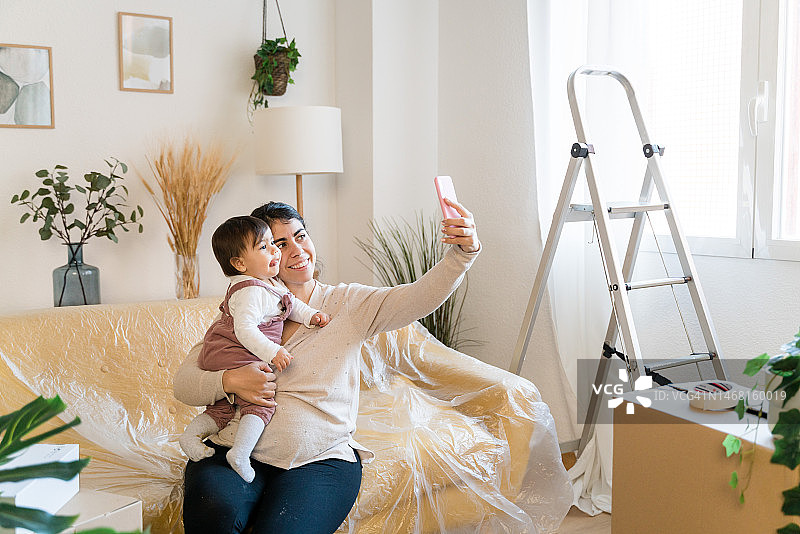 女人抱着坐在客厅沙发上的婴儿，在新家自拍图片素材