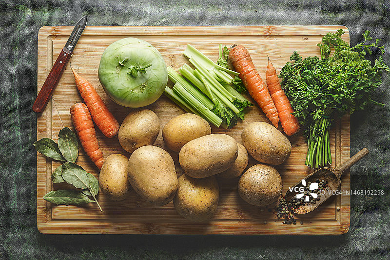 用于土豆汤或蔬菜汤的各种生蔬菜配料，在砧板上配有削皮器和调味料。图片素材