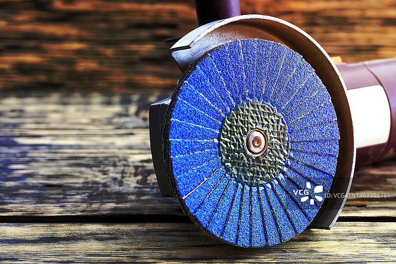 带有花瓣圆形盘刷的角磨机，放在旧木桌上图片素材