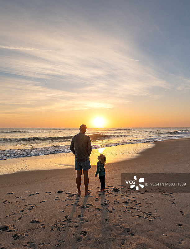 父亲和幼儿女孩在佛罗里达梅里特岛国家野生动物保护区林达海滩欣赏美丽的日出图片素材