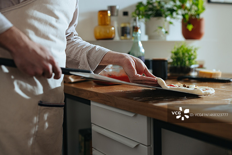 男人将新鲜披萨放在披萨铲上的手部特写照片图片素材