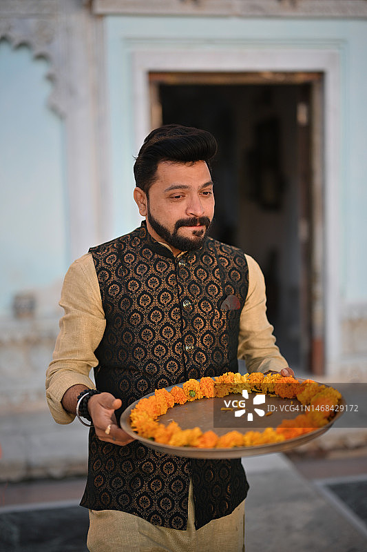 中年男人身穿印度传统服装，手持带有万寿菊花的黄铜盘图片素材