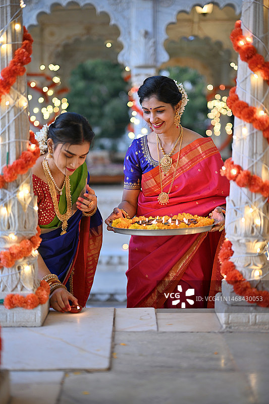 美丽的印度妇女穿着纱丽，用油灯（Diya）装饰大理石凉亭，为传统节日做准备图片素材