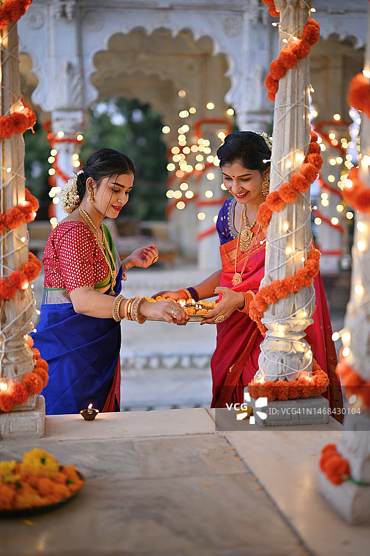 美丽的印度妇女穿着纱丽，用油灯（Diya）装饰大理石凉亭，为传统节日做准备图片素材