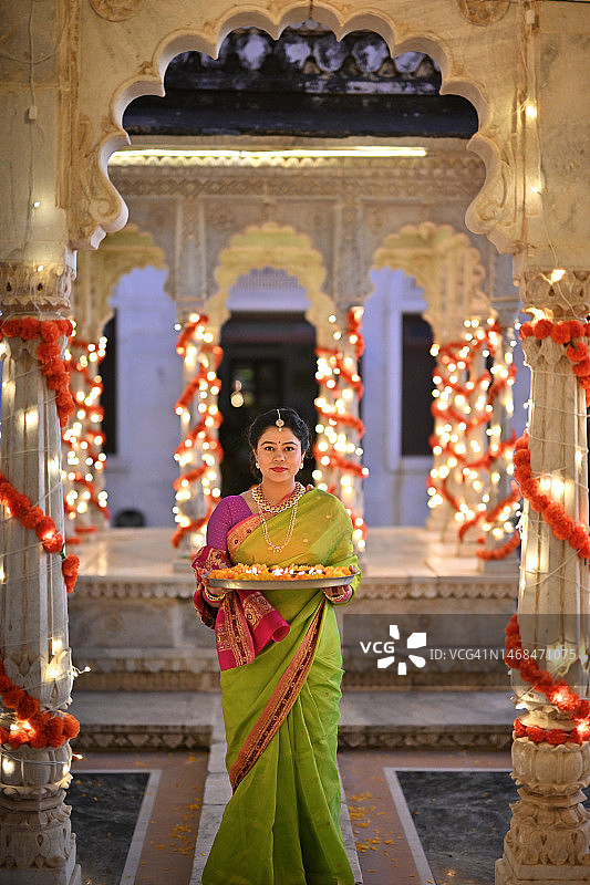 身穿纱丽、手持油灯（Diya）盘、在宫殿大理石亭阁看向镜头的印度中年美丽女性图片素材
