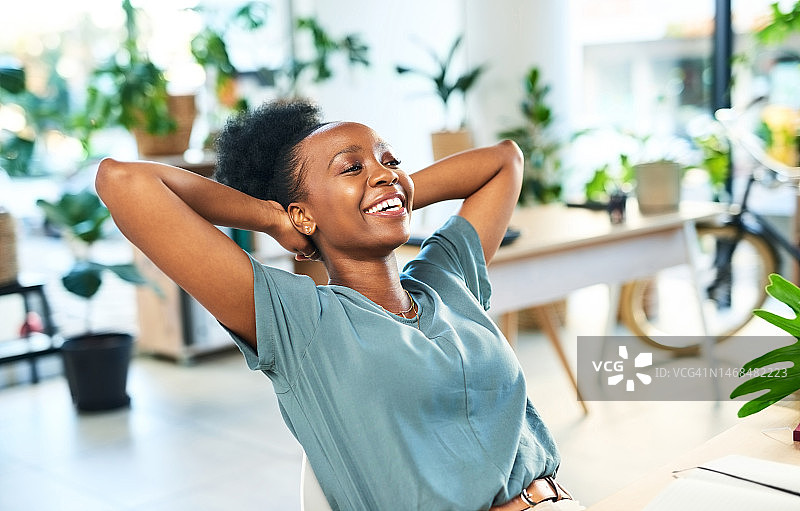黑人女性在办公室伸展放松，轻松完成项目，实现目标，面带微笑，憧憬商业未来。双手抱头，快乐的员工完成工作目标，充满幸福感和动力图片素材