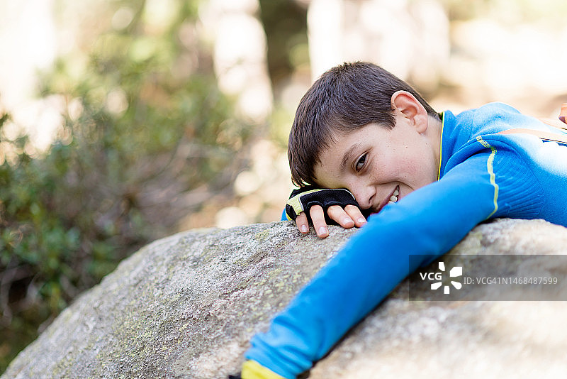 在森林岩石上看着镜头的微笑男孩图片素材