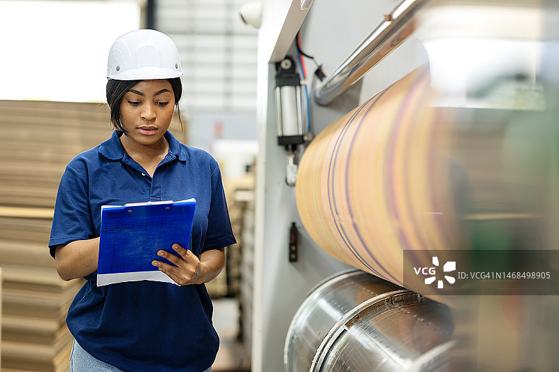 优化设备利用率和机器监控，以支持生产计划。一位非洲裔美国女生产工程师在每日、每周或每月的运营报告清单上做笔记，以提高印刷厂的生产力图片素材