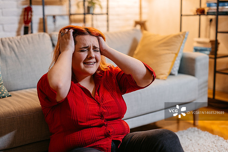 夜晚坐在家地板上的悲伤年轻女人图片素材
