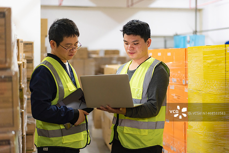 两名仓库管理人员使用笔记本电脑清点货物数量图片素材