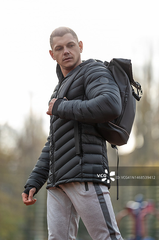 健壮男人背背包在户外运动场摆姿势图片素材