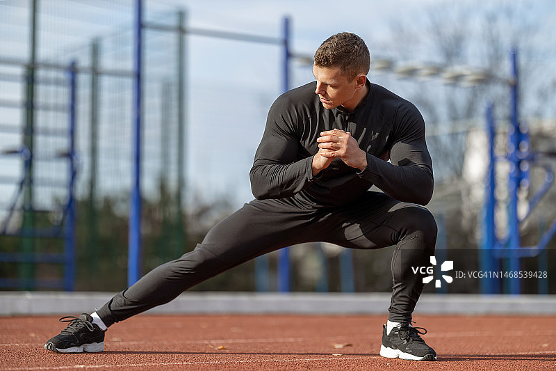 身穿黑色运动服的健壮男人在训练前伸展肌肉图片素材