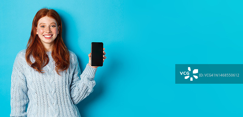 微笑的红发女模特展示智能手机屏幕，手持图片素材