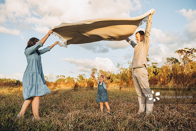 年轻夫妇和可爱的两岁女儿在挥舞的毯子下图片素材