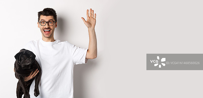 戴眼镜的年轻男人抱着他的黑色巴哥犬挥手图片素材