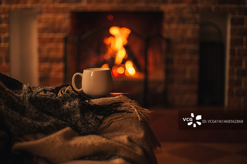 放在椅子上的热茶杯，椅子上盖着羊毛毯，舒适的客厅里有壁炉，美国图片素材