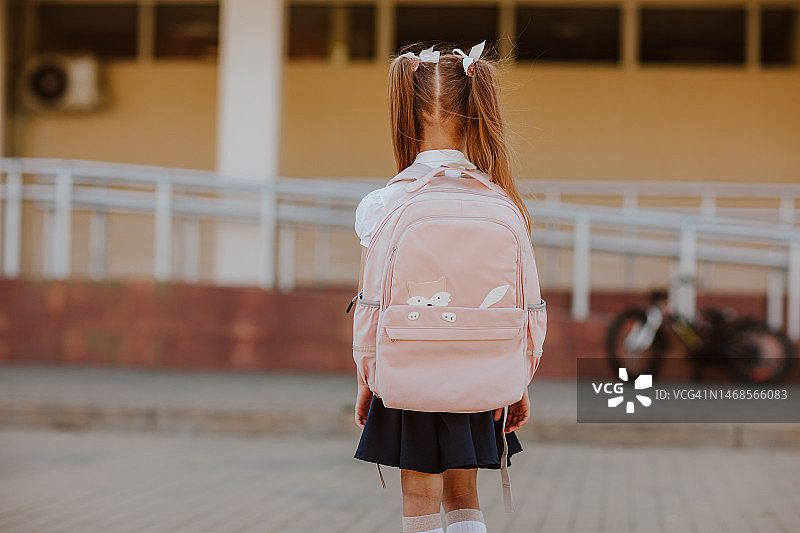 穿着蓝白色校服、背着粉色书包的女孩在校园里摆姿势图片素材