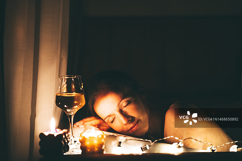 美丽的女人在热浴缸里放松，晚上喝着一杯葡萄酒，点着蜡烛图片素材