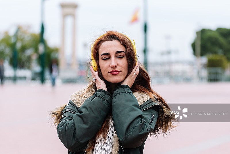 戴着黄色耳机在城市街道上听音乐的红发女孩图片素材