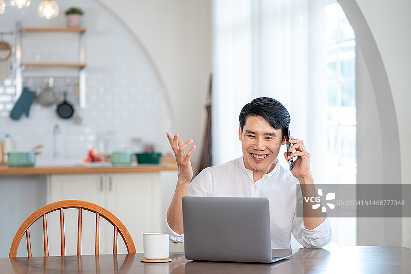 快乐的亚洲男人在家里的客厅里使用笔记本电脑工作。图片素材