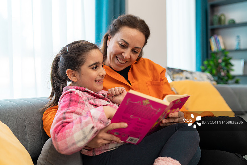 母亲和女儿在家中沙发上读书图片素材