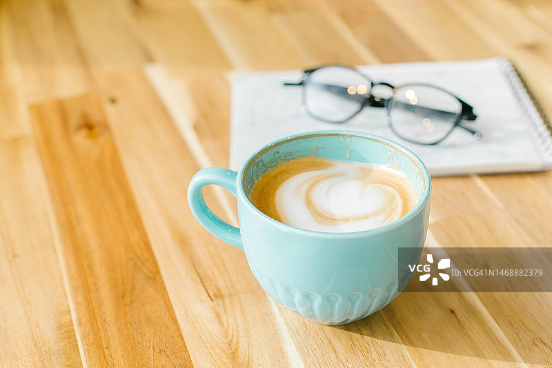 蓝色咖啡杯中的卡布奇诺咖啡、眼镜和笔记本图片素材