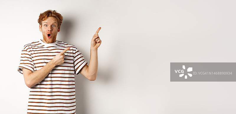 兴奋的红发卷发男子展示促销优惠，看起来很惊讶图片素材