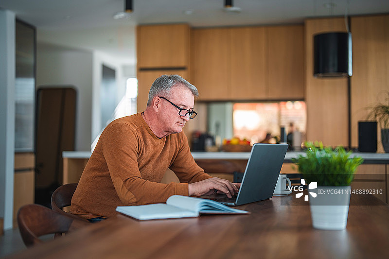 在家使用笔记本电脑的灰发白人男性图片素材