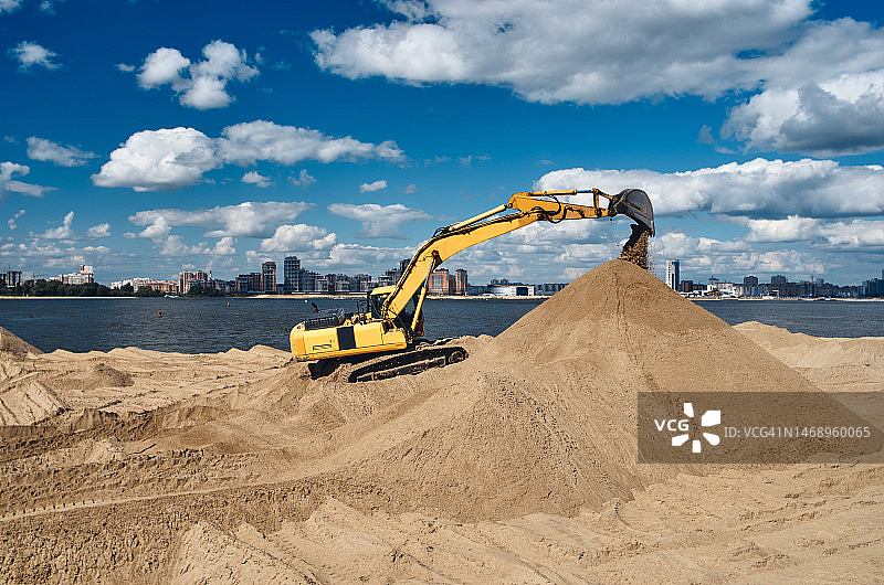城市河岸边的挖掘机在挖掘沙滩上的沙子图片素材