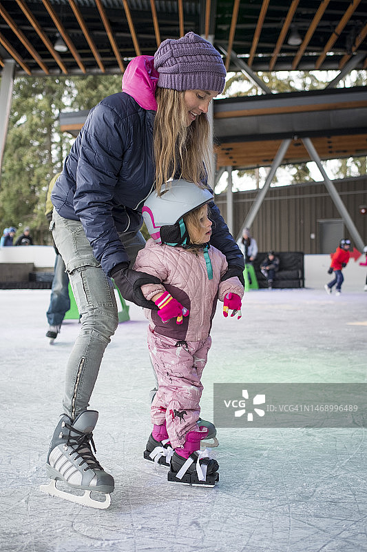 冬天，小女孩和妈妈在溜冰场学习滑冰图片素材