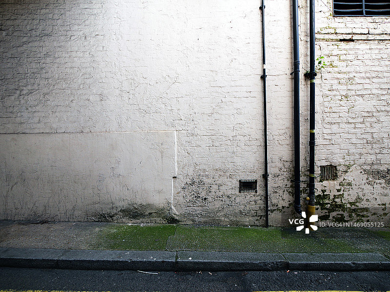 伦敦带管道、通风网格和路面的风化白色砖墙图片素材