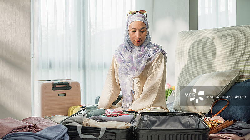 年轻的亚洲穆斯林女性在家中卧室整理行李箱，准备旅行度假图片素材