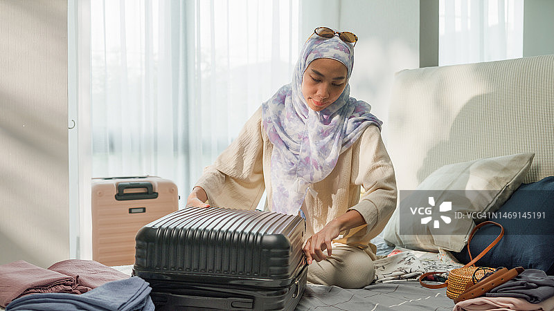 年轻的亚洲穆斯林女性在家中卧室整理行李箱，准备旅行度假图片素材