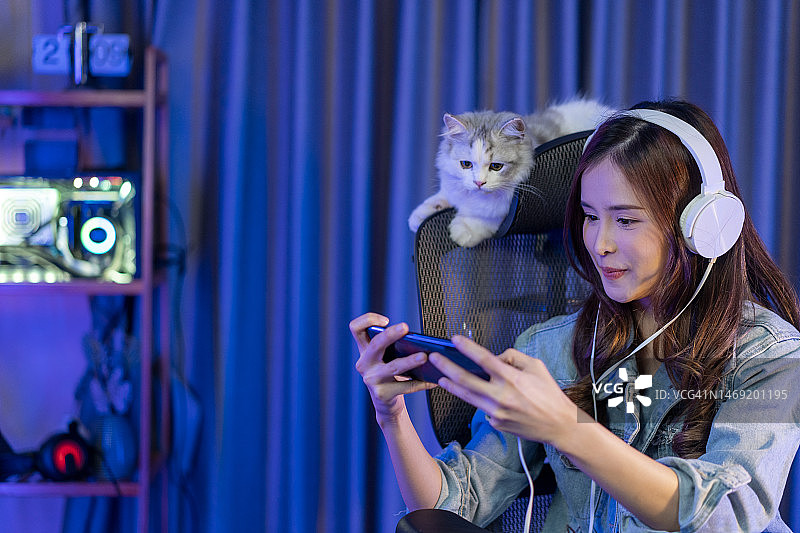 一位兴高采烈的年轻亚洲女性戴着耳机，用智能手机玩在线电竞游戏图片素材