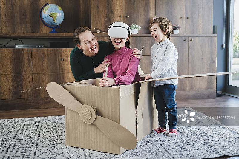 母亲和孩子们在纸板箱飞机里玩虚拟现实模拟器图片素材