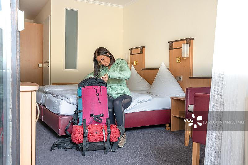 徒步旅行的迷人女子坐在酒店的床上，看着她的大背包，德国黑森林巴特维尔德巴德图片素材