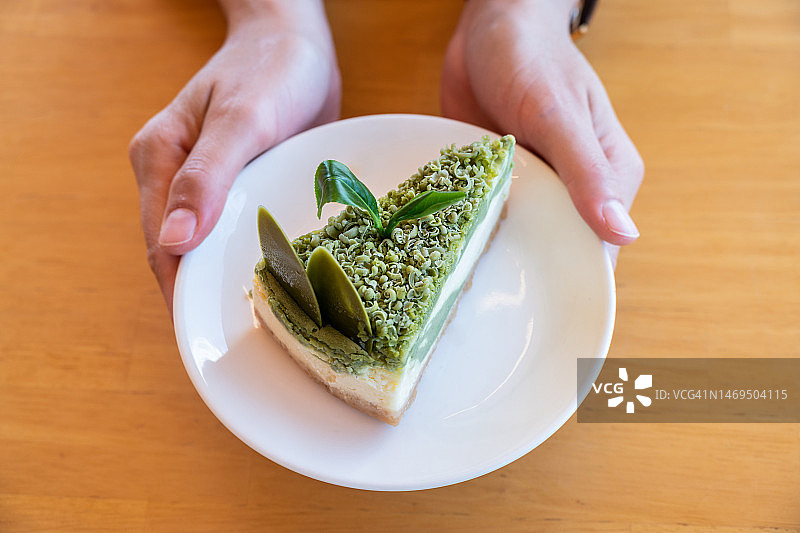 在吃抹茶蛋糕前，手捧抹茶蛋糕盘子的局部照片。图片素材