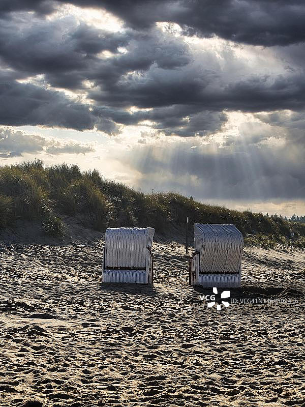 德国北弗里西亚于特苏姆秋季沙丘前的两把沙滩椅，阳光穿透云层图片素材