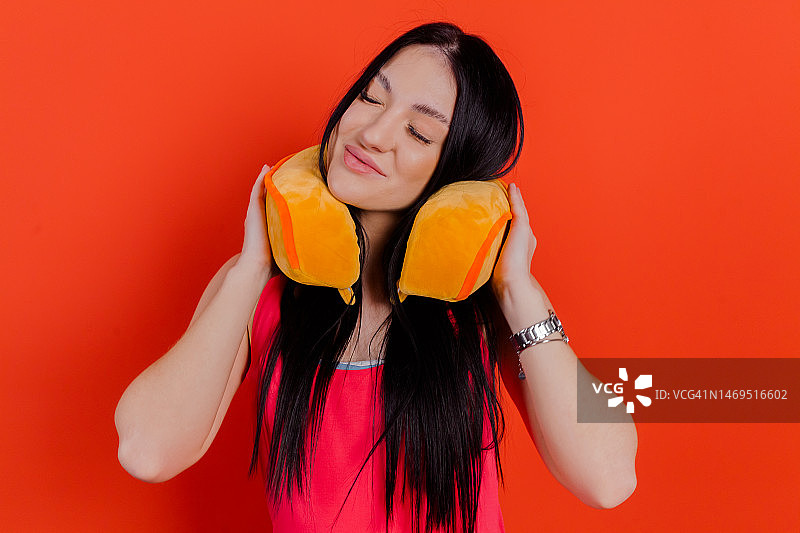 特写：女孩舒适地靠在旅行枕上，背景为亮红色图片素材