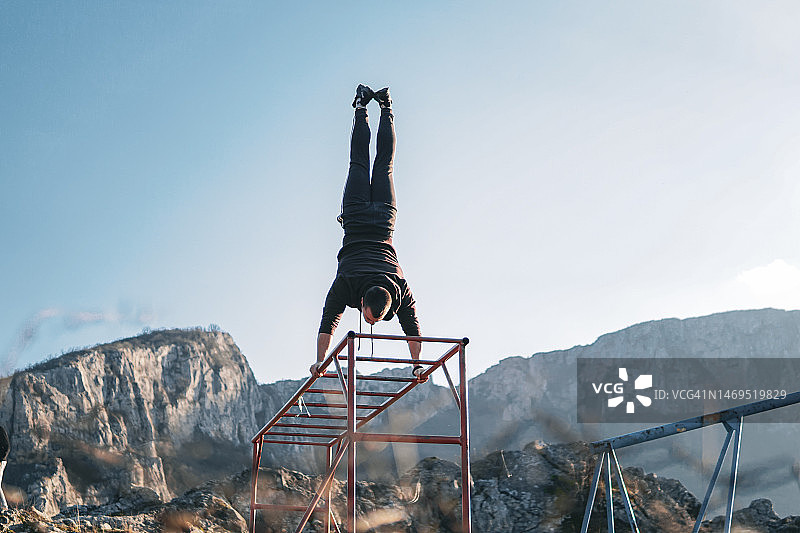 男子在公园的单杠上做倒立图片素材