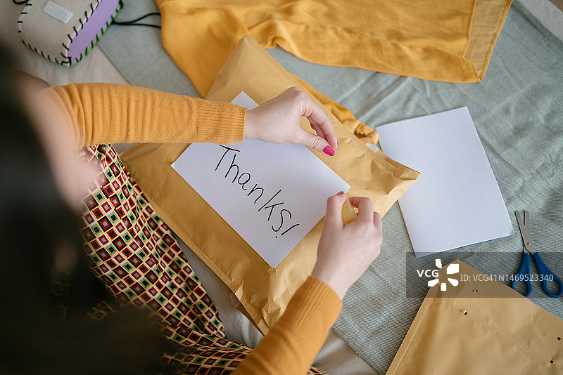 女人将“感谢”标签贴在准备发货的大信封上，二手销售概念图片素材
