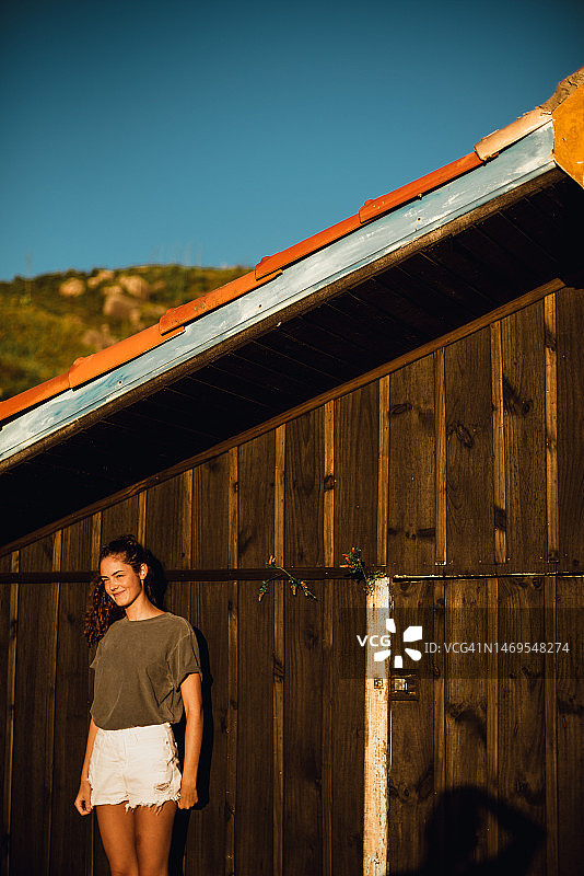 穿灰色T恤年轻女人木屋前沐浴晨光图片素材