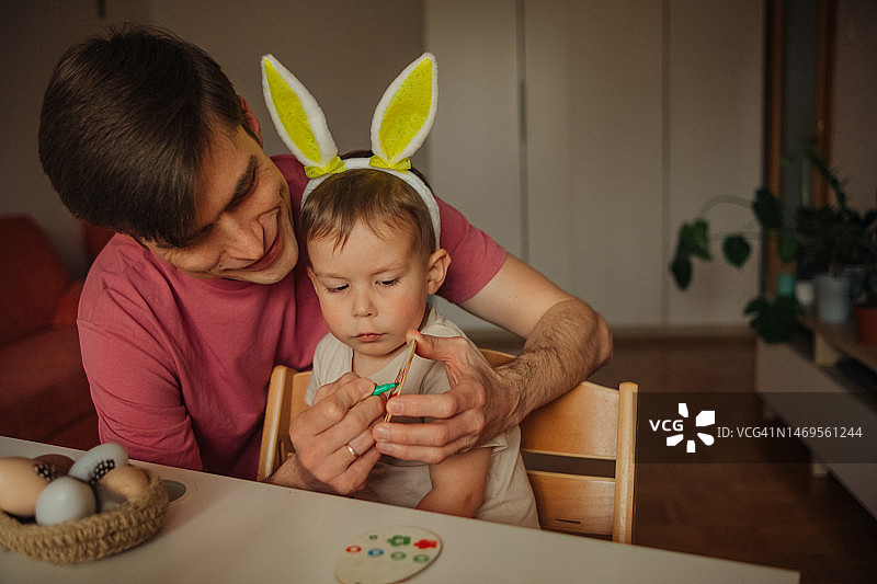 爸爸和孩子戴着兔子耳朵头饰装饰复活节彩蛋图片素材