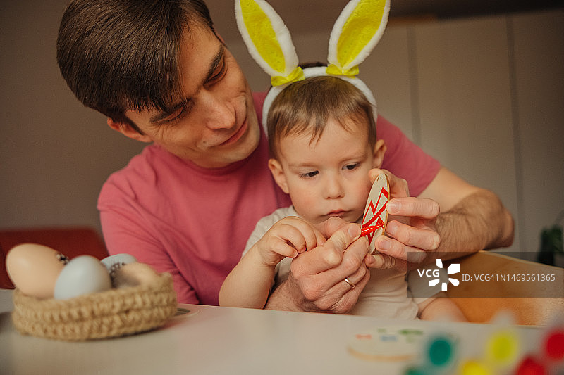 爸爸和孩子戴着兔子耳朵头饰装饰复活节彩蛋图片素材