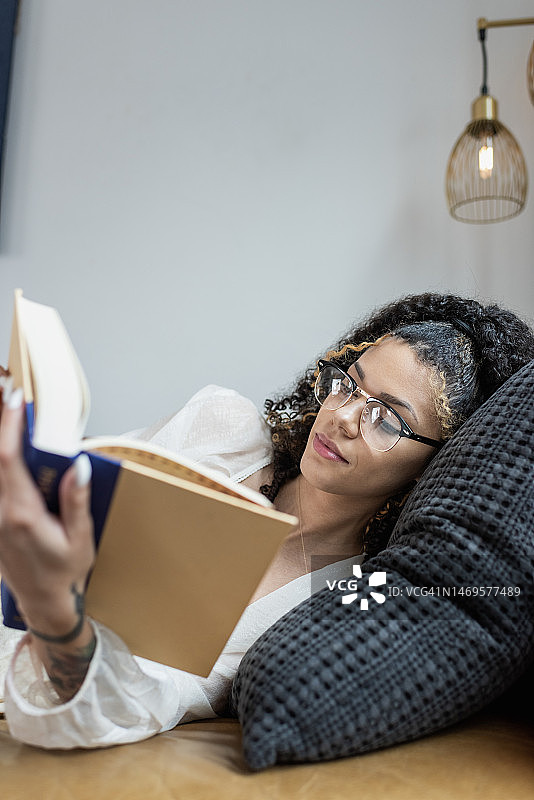 年轻女子斜倚在沙发上看书图片素材