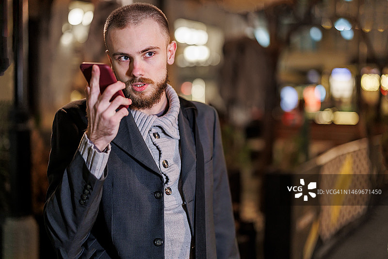 年轻男人在夜晚的城市街道上用手机交谈图片素材