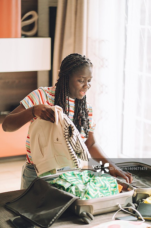 微笑的女人在沙发上从行李箱里取出衣服图片素材