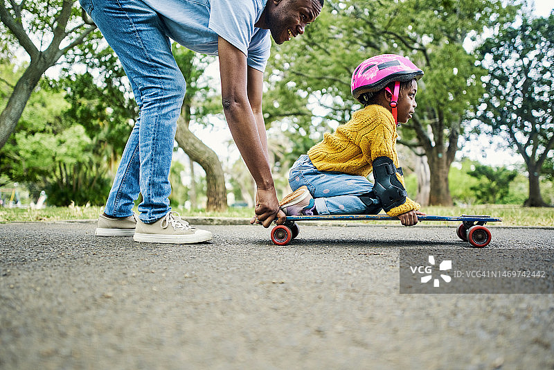 户外公园：父亲教女儿玩滑板图片素材