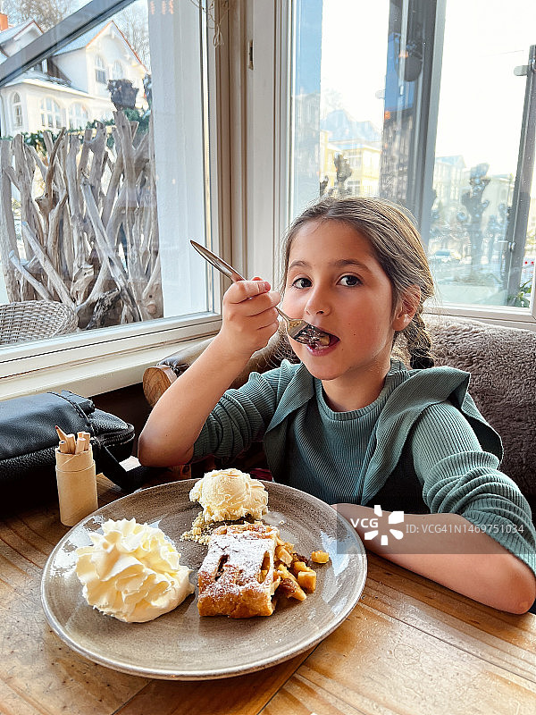 在咖啡馆吃苹果卷配冰淇淋和奶油的白人女孩图片素材