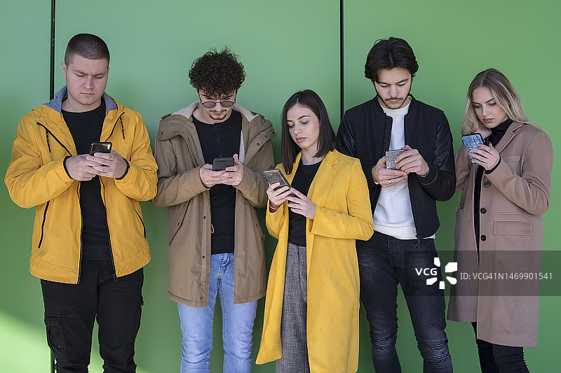 一群年轻人在户外使用智能手机 - 千禧一代享受社交媒体新潮流 - 沉迷科技的年轻人 - 绿色背景图片素材